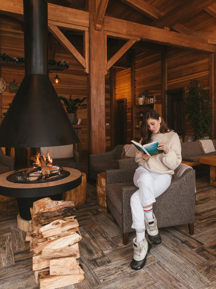 Woman reading in a warm, wooden cabin by the fireplace, evoking relaxation and comfort.